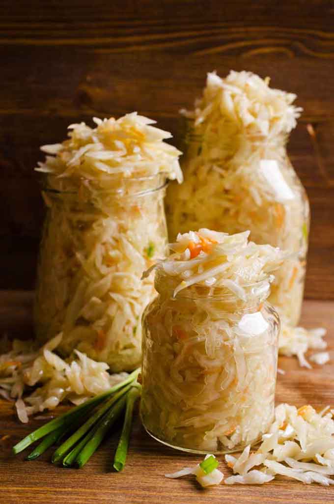 Three jars overflowing with sauerkraut with spring onions beside the jar. | MakeSauerkraut.com