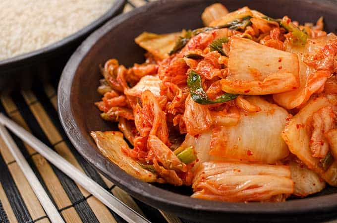 Kimchi serving inside a black bowl with chopsticks to the side. | MakeSauerkraut.com