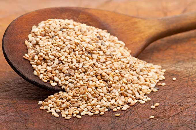 Toasted sesame seeds being poured to the surface from a wooden spoon. | MakeSauerkraut.com