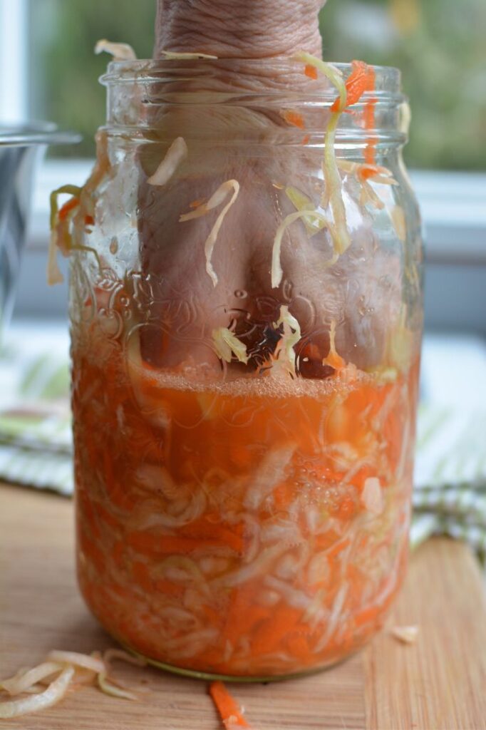 hand pushing down sauerkraut in a jar | MakeSauerkraut.com