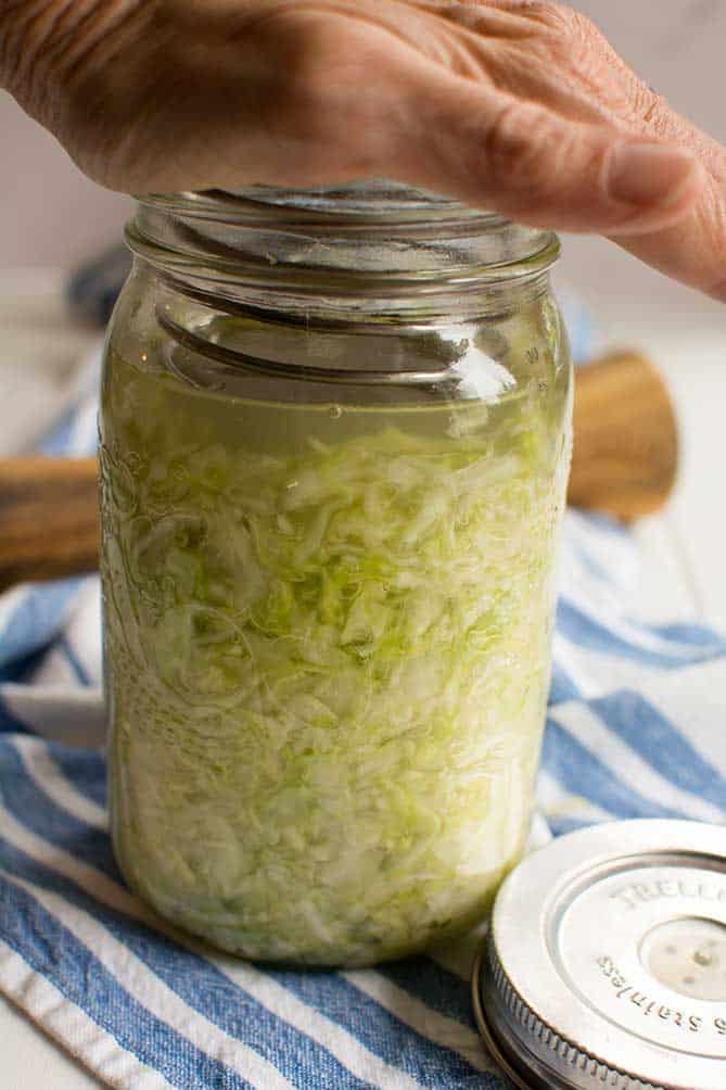 The PickleHelix being pushed into a jar of fermenting sauerkraut. with the palm of a hand. | MakeSauerkraut.com