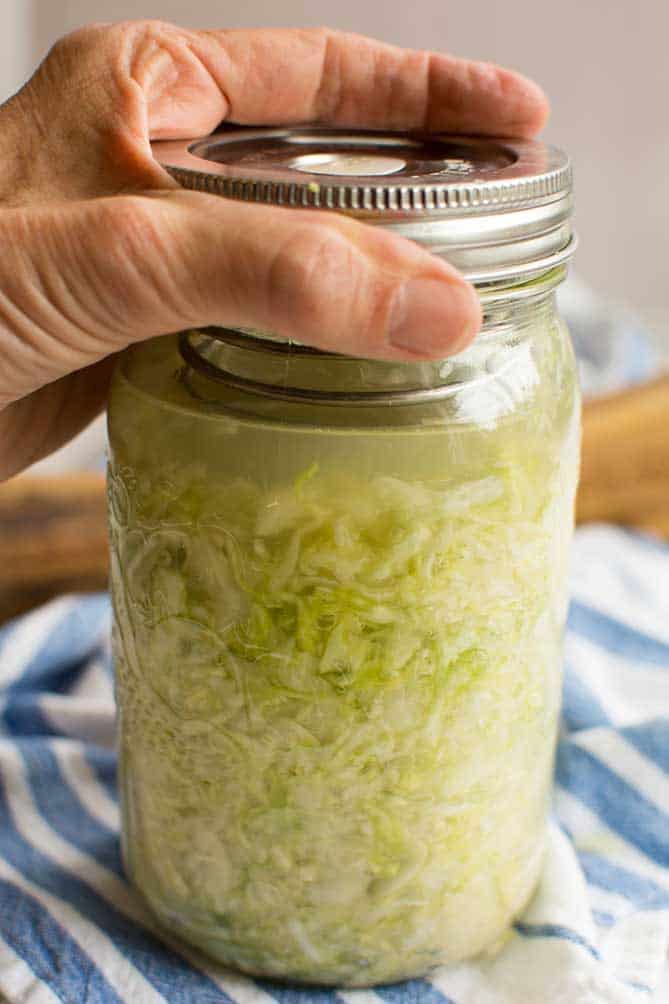 Hand screwing the metal lid to a fermenting sauerkraut with the PickleHelix inside the jar. | MakeSauerkraut.com