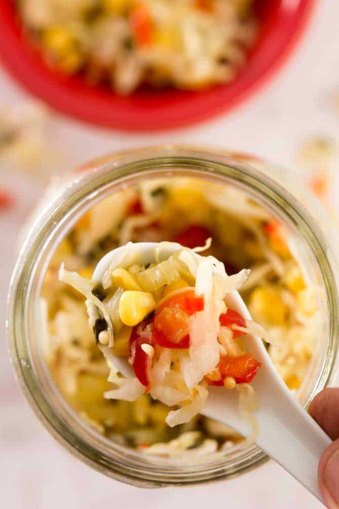 Dipping a spoon into a jar of sauerkraut Corn Relish. | Makesauerkraut.com