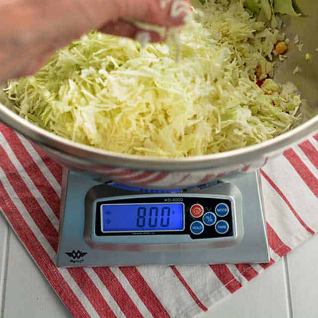 Hand adding sliced cabbage to metal bowl on My-Weigh KD-8000 scale. | Makesauerkraut.com