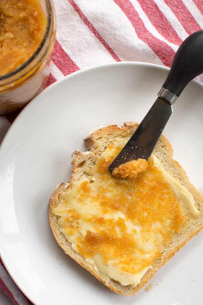 Morning toast on white plate spread with fermented garlic paste using a butter knife. | MakeSauerkraut.com