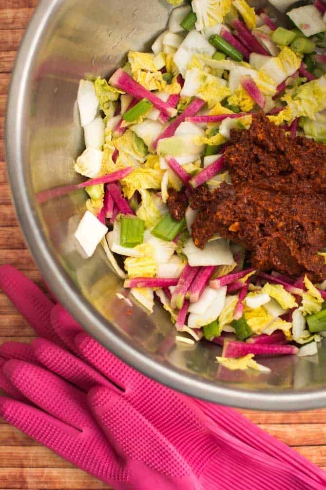 Bowl with cabbage, radish and red pepper paste for kimchi with pink rubber gloves to the side. | MakeSauerkraut.com