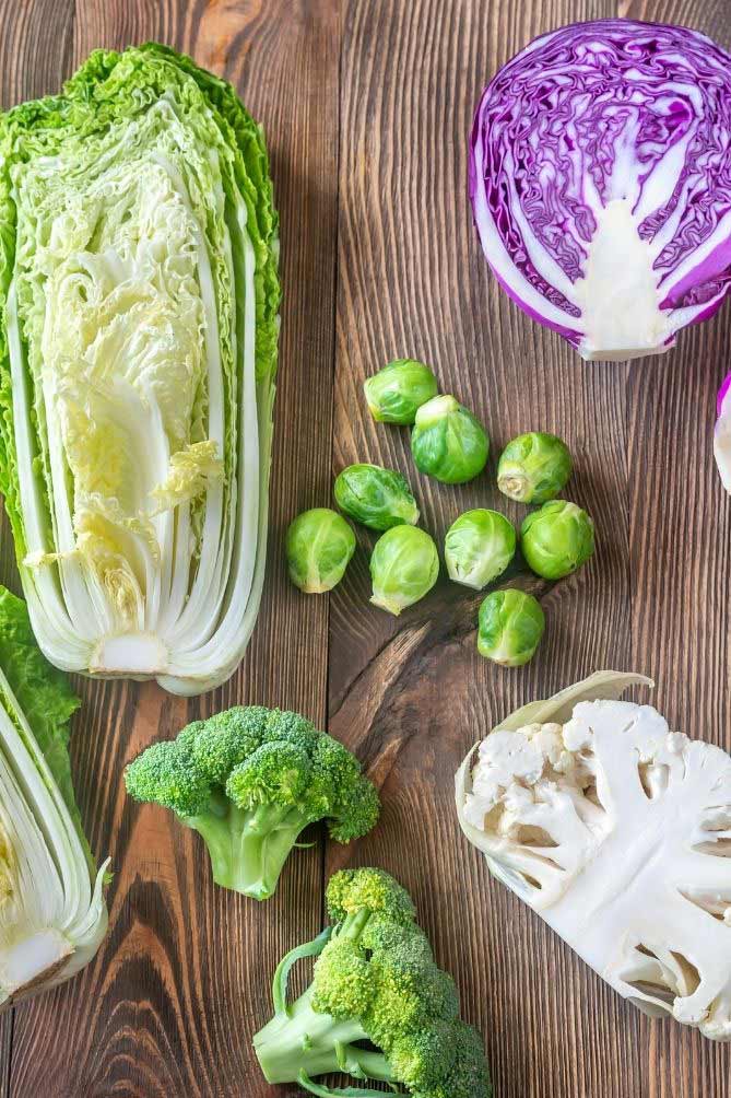 Chinese cabbage, 2 broccoli heads, half cauliflower, brussels sprouts, and half a purple cabbage laid out against wooden table. | MakeSauerkraut.com