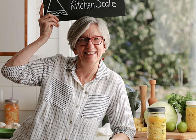 Woman in striped shirt holding Kitchen Scale sign above hear. | MakeSauerkraut.com