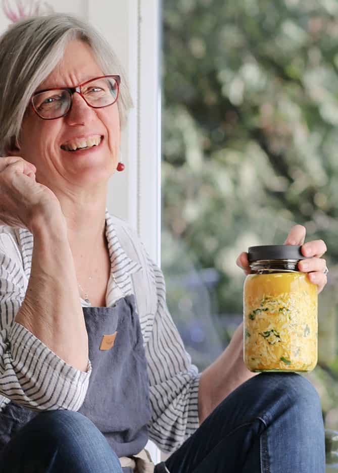 Woman sitting with jar of sauerkraut on knee. | MakeSauerkraut.com