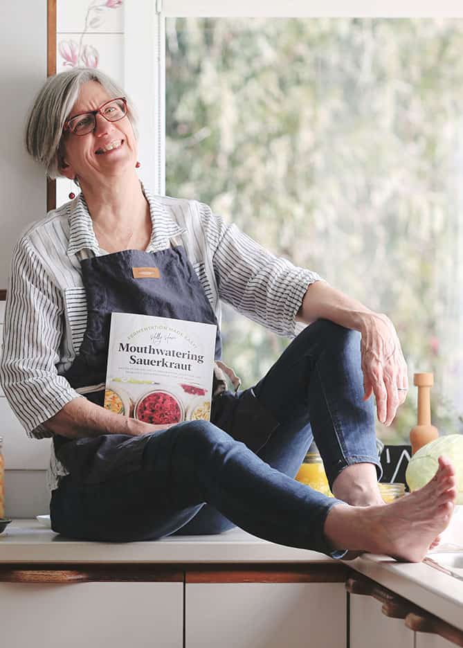 Woman sitting on counter holding Mouthwatering Sauerkraut book on lap. | MakeSauerkraut.com