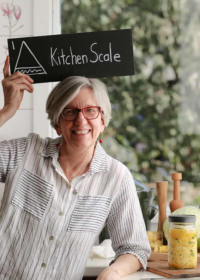 Woman in striped shirt holding Kitchen Scale sign above hear. | MakeSauerkraut.com