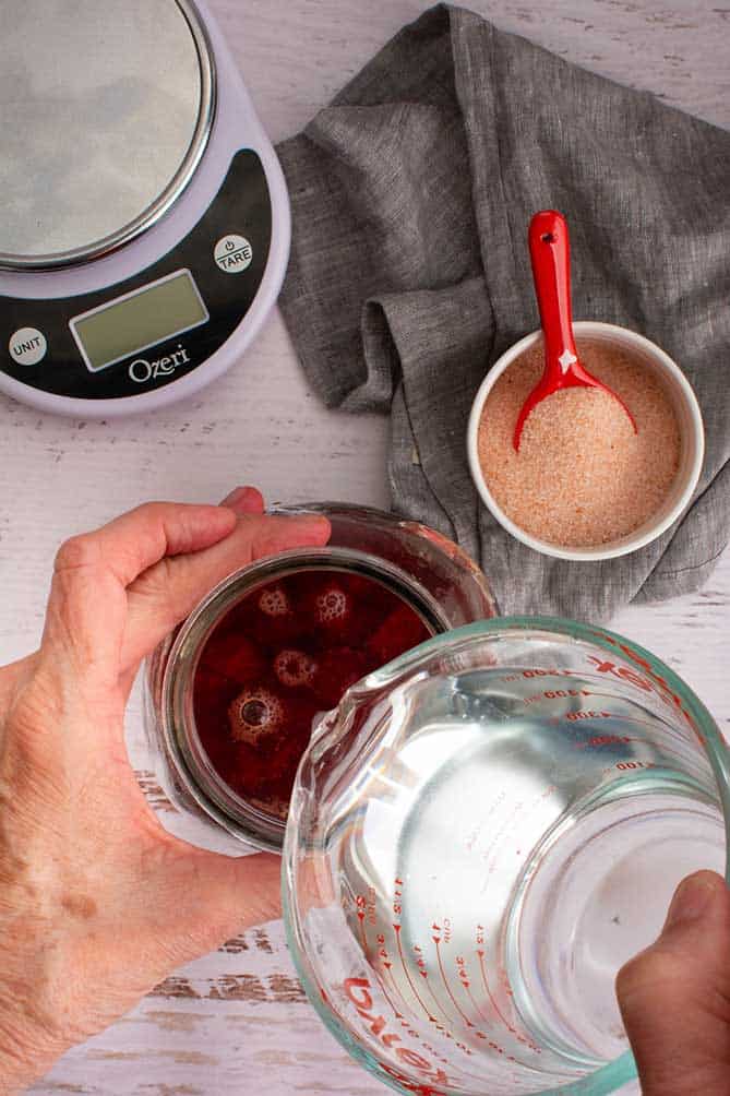 Water being poured into jar of chopped beets. | MakeSauerkraut.com