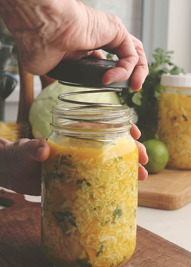 Lid screwed onto jar of sauerkraut with spring weight. | MakeSauerkraut.com