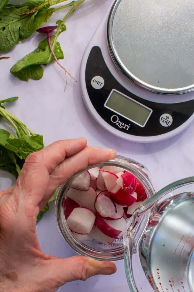 Water poured into a jar of radish chunks. | MakeSauerkraut.com