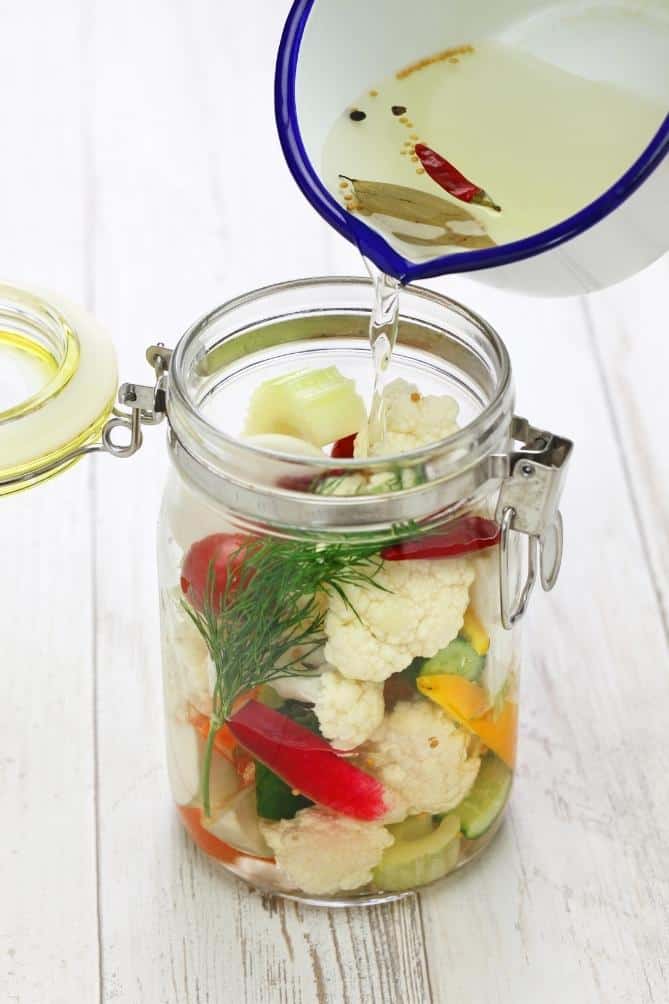 Pouring hot, seasoned vinegar over an open jar of cauliflower to pickle | MakeSauerkraut.com
