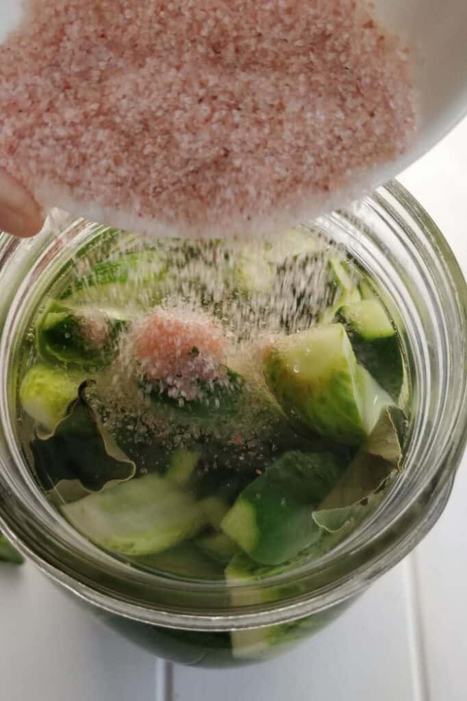 Salt being pouring into a jar packed with cucumber slices. | MakeSauerkraut.com