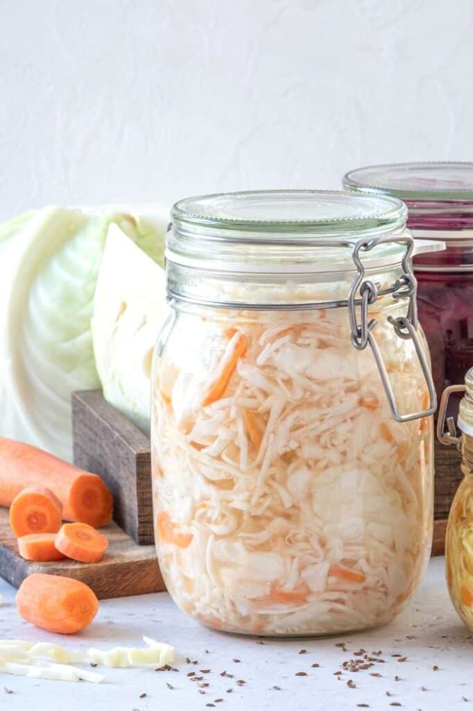 A jar of sauerkraut with carrots and cabbage on the background