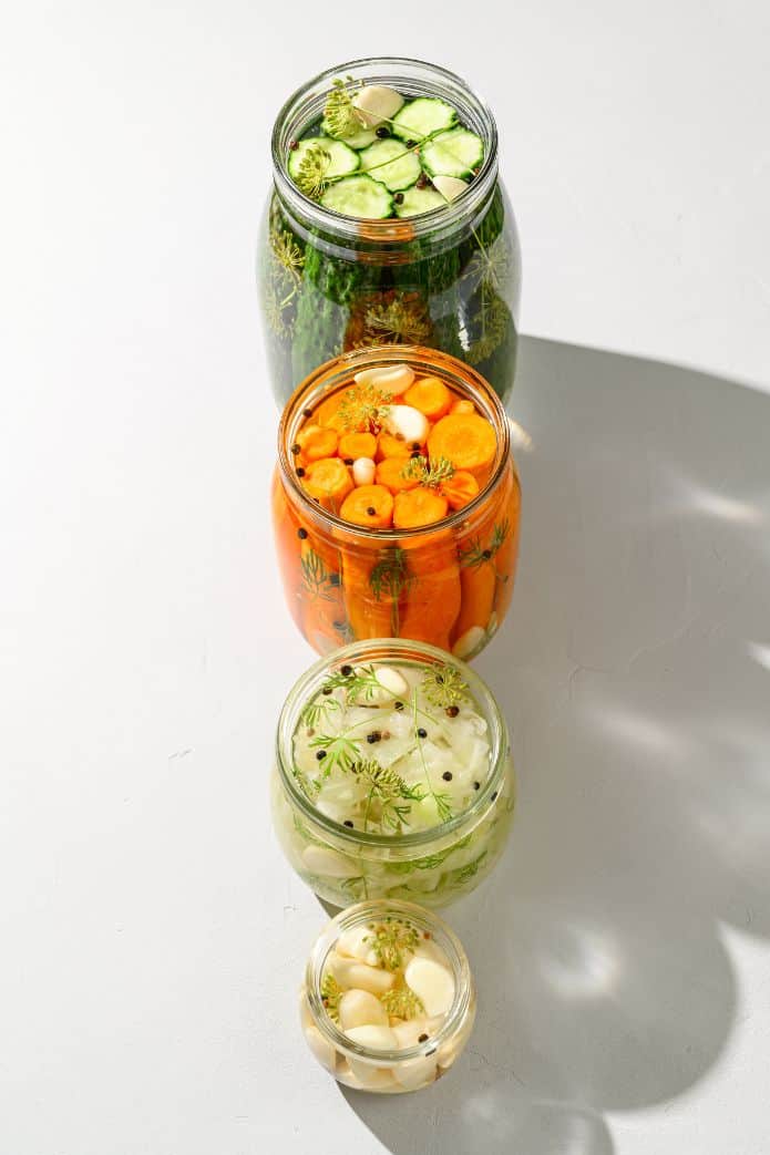 Open jars of pickles, carrots, onions & garlic lined up. | MakeSauerkraut.com