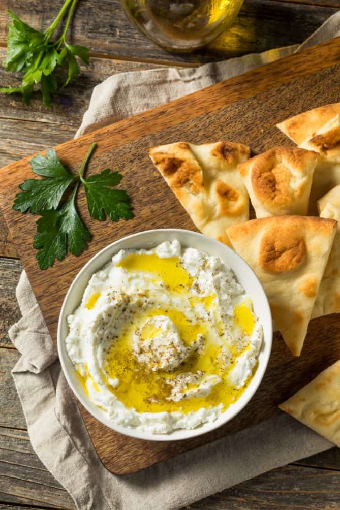 A bowl of yogurt cheese and pita bread on a wooden cutting board. | MakeSauerkraut.com