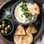 A dark serving plate with bowls of pita bread, olives, and labneh or yogurt cheese. | MakeSauerkraut.com