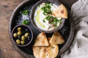 A dark serving plate with bowls of pita bread, olives, and labneh or yogurt cheese. | MakeSauerkraut.com