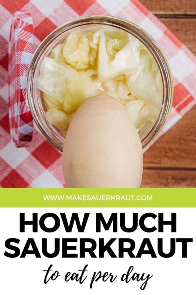 Fermented sauerkraut in a glass jar with a wooden spoon and a napkin with a text overlay How Much Sauerkraut To Eat Per Day | MakeSauerkraut.com.