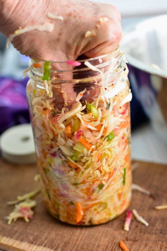 best fermentation tips Woman packing a jar with sliced cabbage and grated carrot mixture for making sauerkraut. | MakeSauerkraut.com.