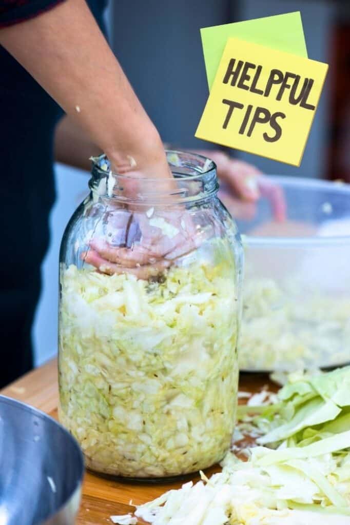 A womans hand packing the jar of sauerkraut. | makesauerkraut.com